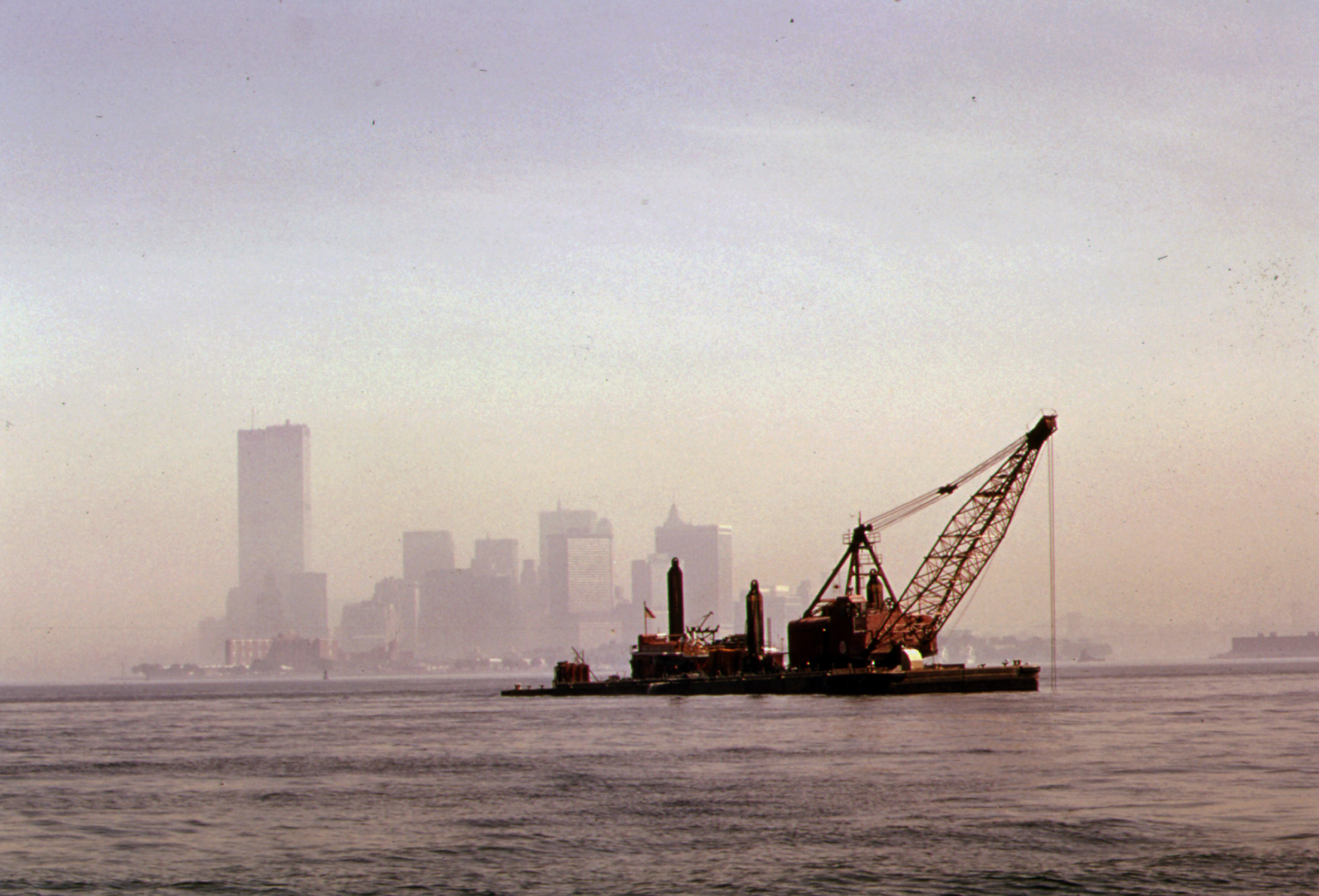 A crane dredge in water in front of a hazy city skyline